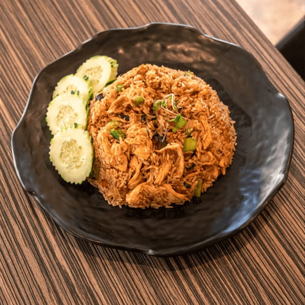 Thai fried rice with chicken, green onions, and cucumber slices on a black plate.