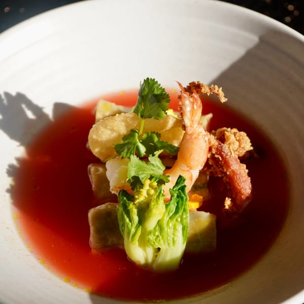 Thai dish with shrimp, crispy pork, vegetables, and cilantro in a vibrant red broth.