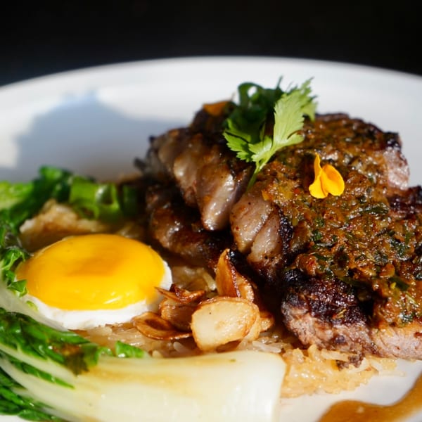 Thai grilled steak with a fried egg, bok choy, and crispy garlic on rice.