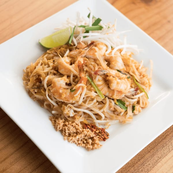 Shrimp Pad Thai with bean sprouts, lime, crushed peanuts, and chili flakes on a white plate.