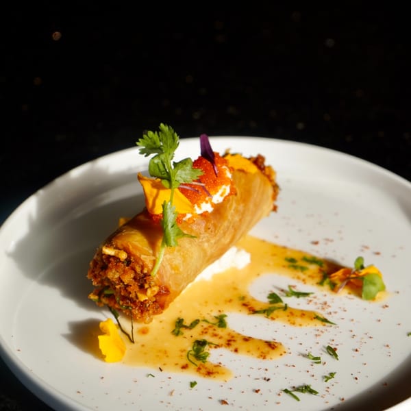Crispy Thai spring roll with white sauce, orange roe, cilantro, and edible flowers on a white plate.