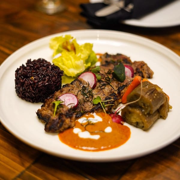 Grilled Thai beef with black rice, green salad, radishes, and a red curry sauce.