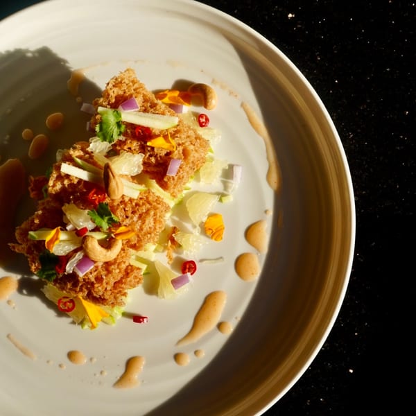 Crispy Thai salad with cashews, red onion, chili, and edible flowers on a white plate.