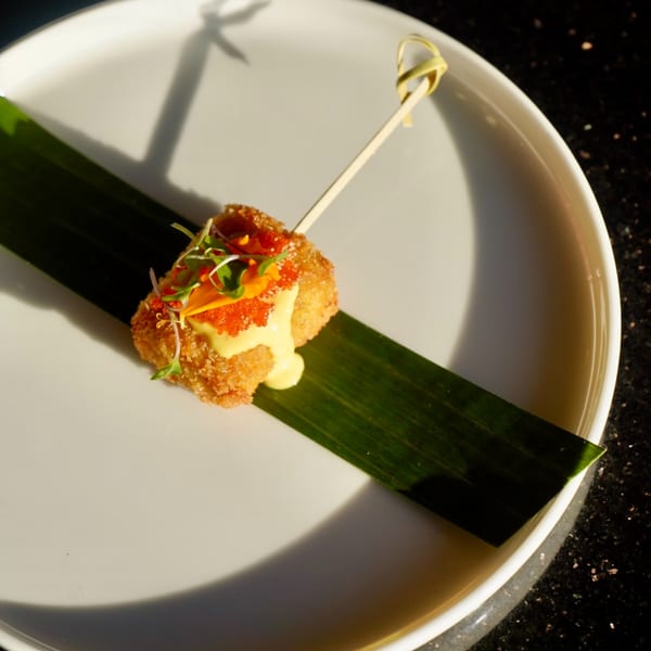 Crispy Thai appetizer with orange roe, yellow sauce, and microgreens on a banana leaf.