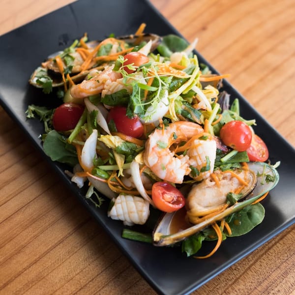 Thai seafood salad with shrimp, mussels, squid, cherry tomatoes, and greens on a black plate.