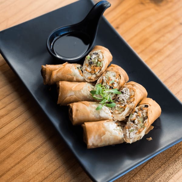 Crispy Thai spring rolls, some cut open to show vegetable and meat filling, with dipping sauce.