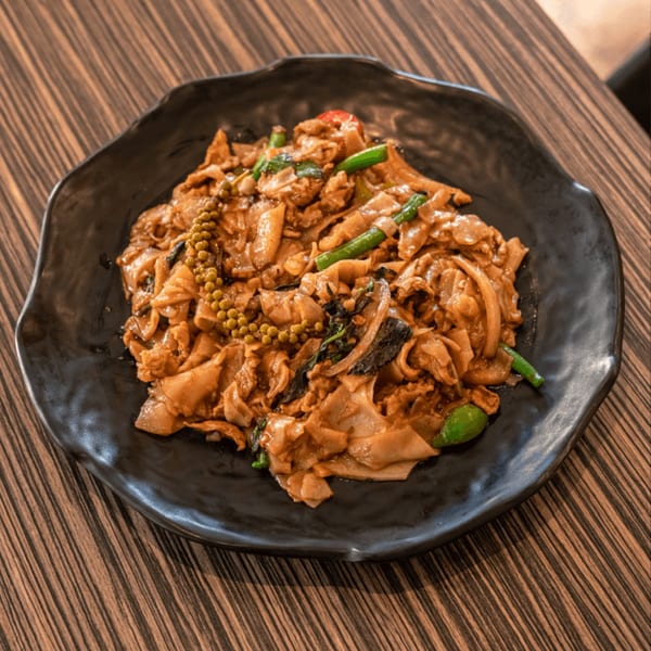 Spicy Thai drunken noodles with wide rice noodles, green peppercorns, and vegetables on a black plate.