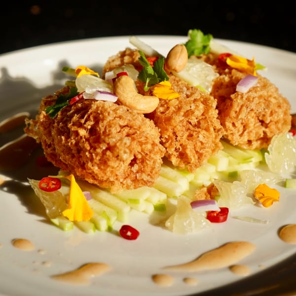 Crispy Thai fried shrimp cakes with cashews, herbs, and chili on a white plate.